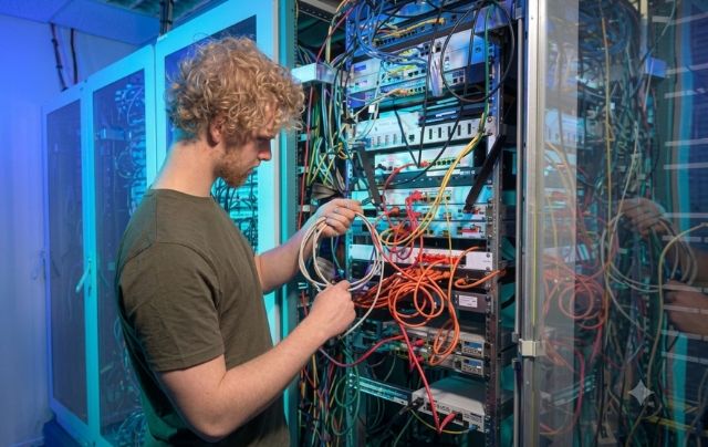 IT technician managing multicolored network cabling and patch panels in a Houston server room rack